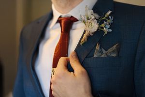 Close-up detail of a navy suit with red tie and white floral boutonniere being adjusted.