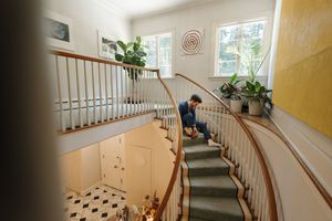 An elegant curved staircase with white railings and grey carpeting leads upward in a bright interior with yellow walls and plants.