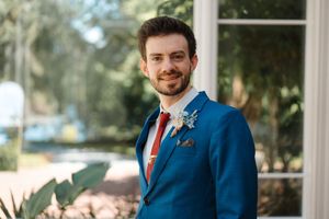 Groomsmen in matching navy blue suits and orange ties pose outdoors in a garden setting.
