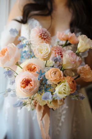 Romantic floral arrangement featuring peach garden roses, pale yellow blooms, and delicate blue delphiniums in soft focus.