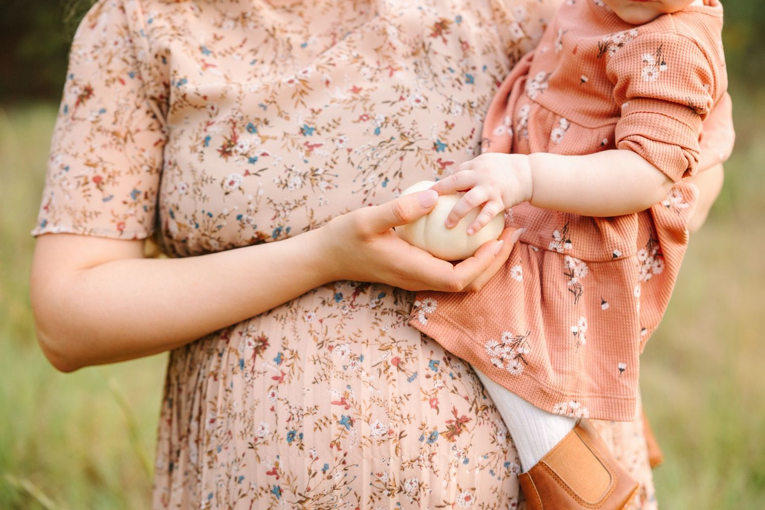 A peach-colored bow adorns a delicate floral dress in a romantic outdoor portrait setting.