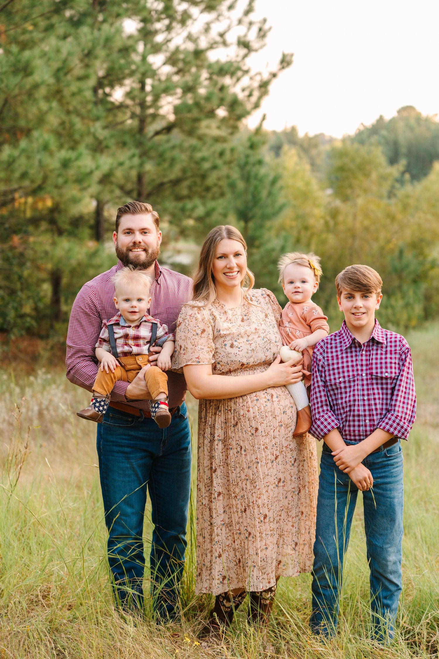 Family poses together in a grassy field wearing coordinated outfits of purple, brown and denim.