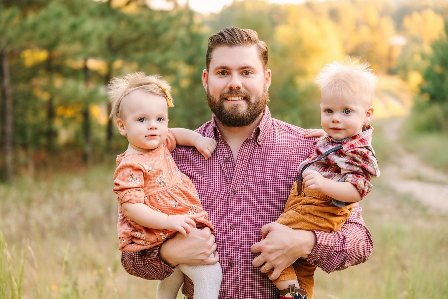 Family portrait in autumn field at golden hour showing affectionate moment with small children.