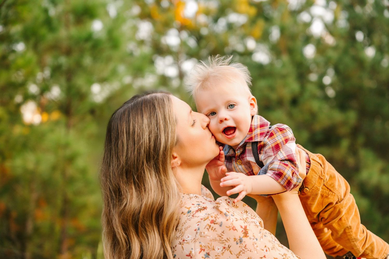 Joyful candid moment between parent and laughing baby against autumn foliage background.