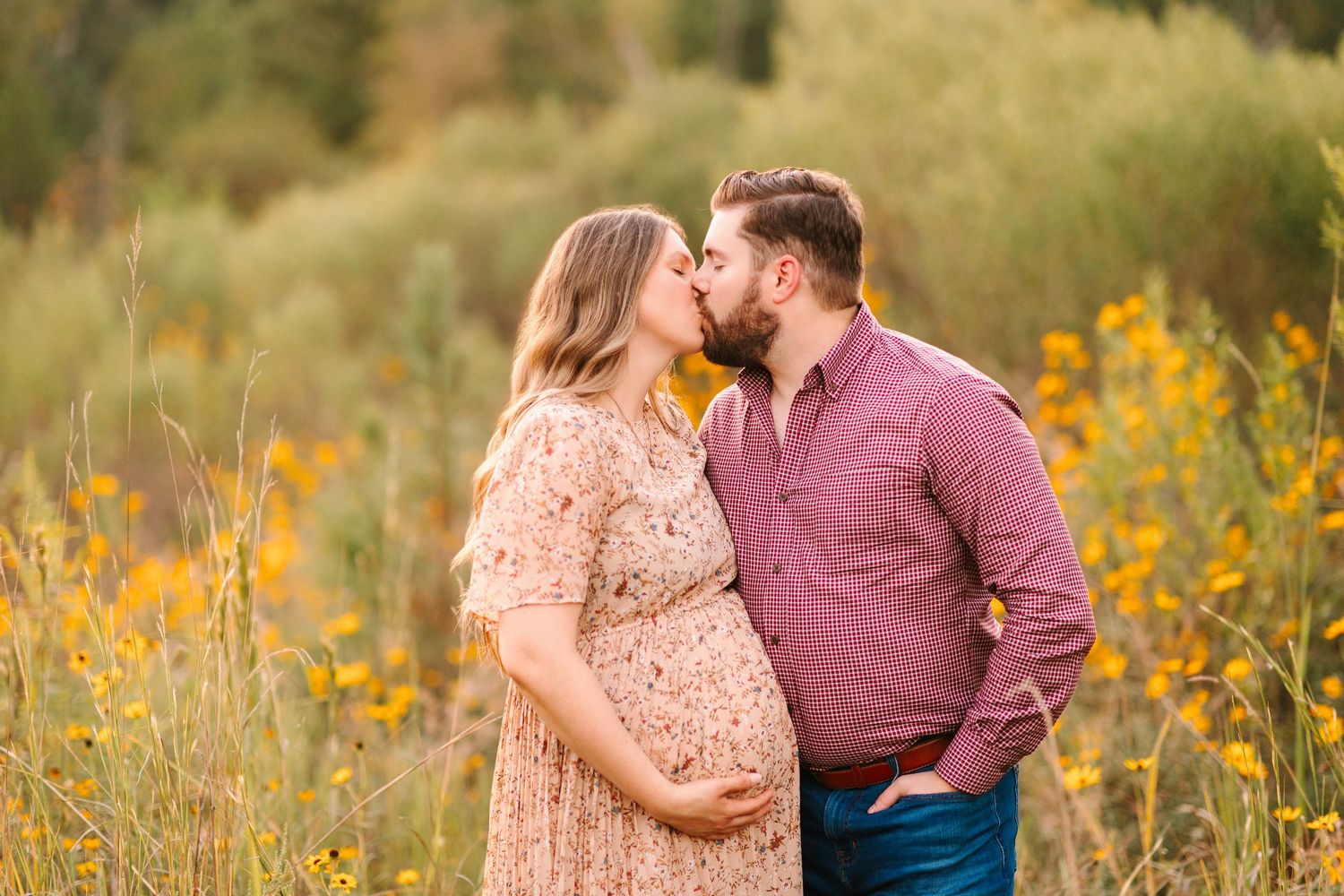 A couple embraces tenderly in a meadow filled with yellow wildflowers during sunset.