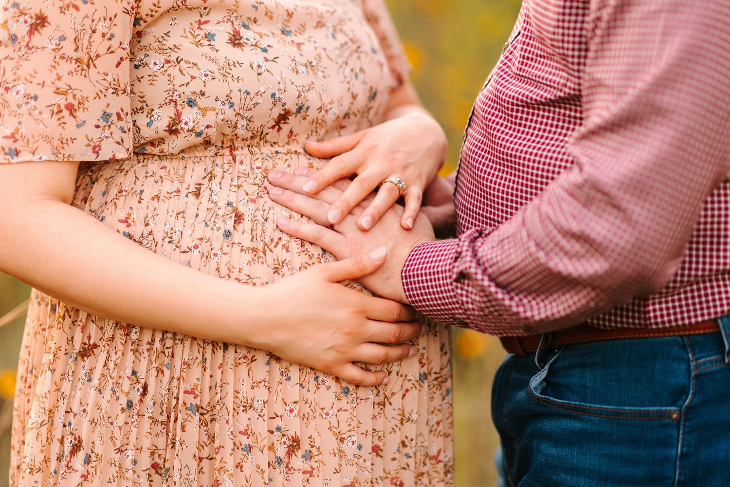 Two hands lovingly rest on a pregnant belly wearing a peach-colored floral dress.