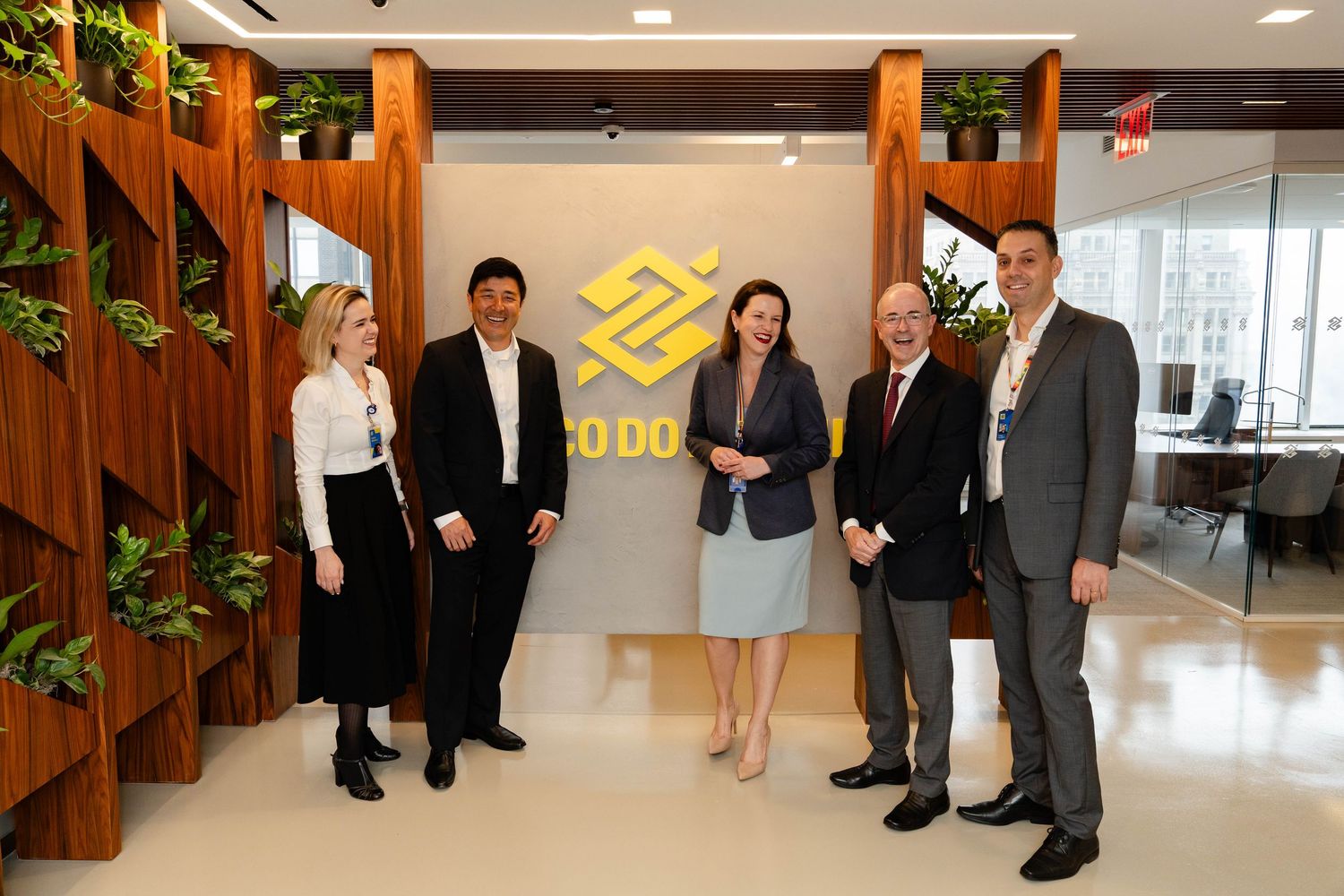 Professional group standing in modern office lobby with wooden dividers and corporation logo on wall.
