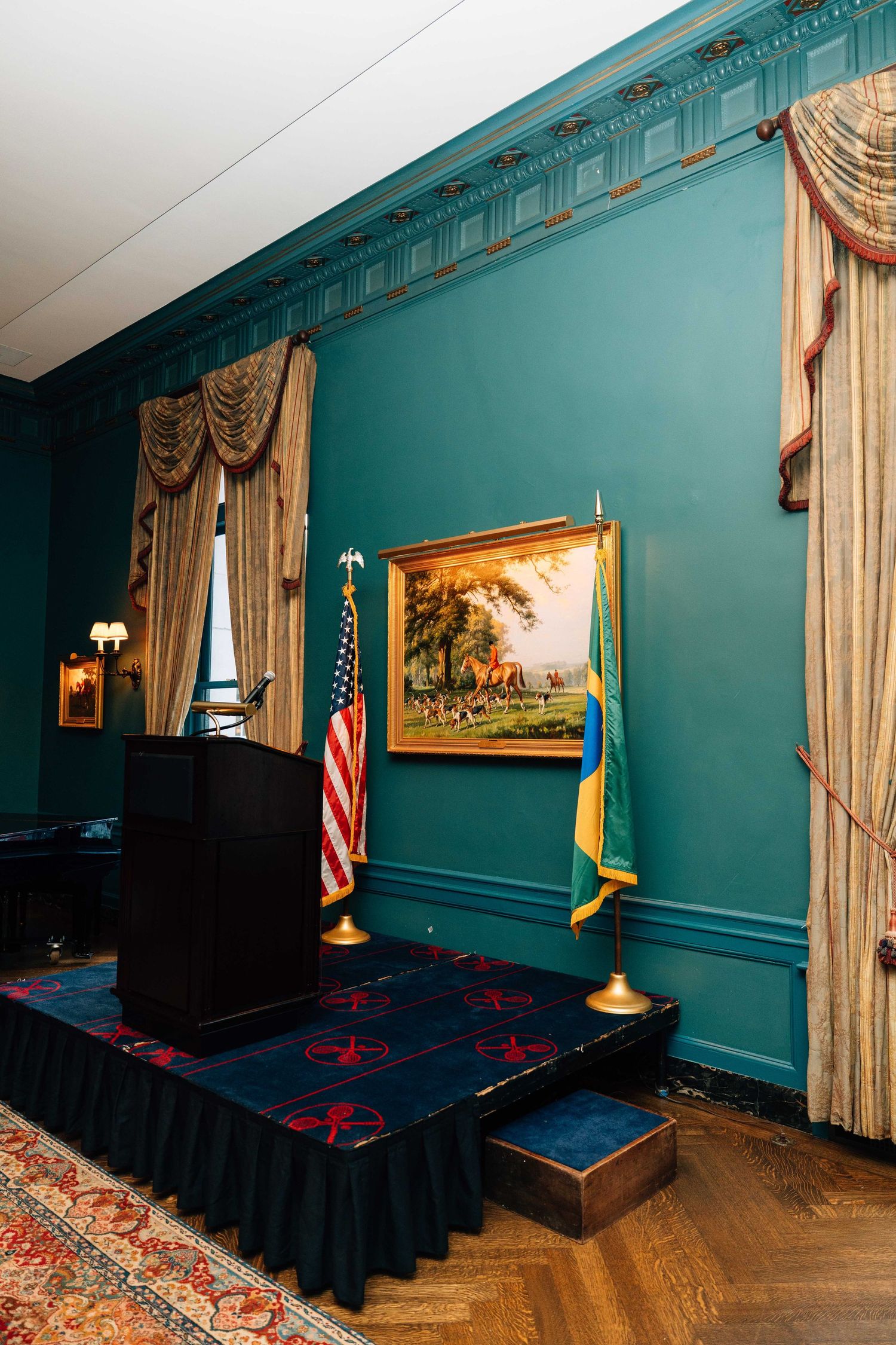 Elegant podium setup in a room with teal walls, gold curtains, American flag, and hardwood floors.