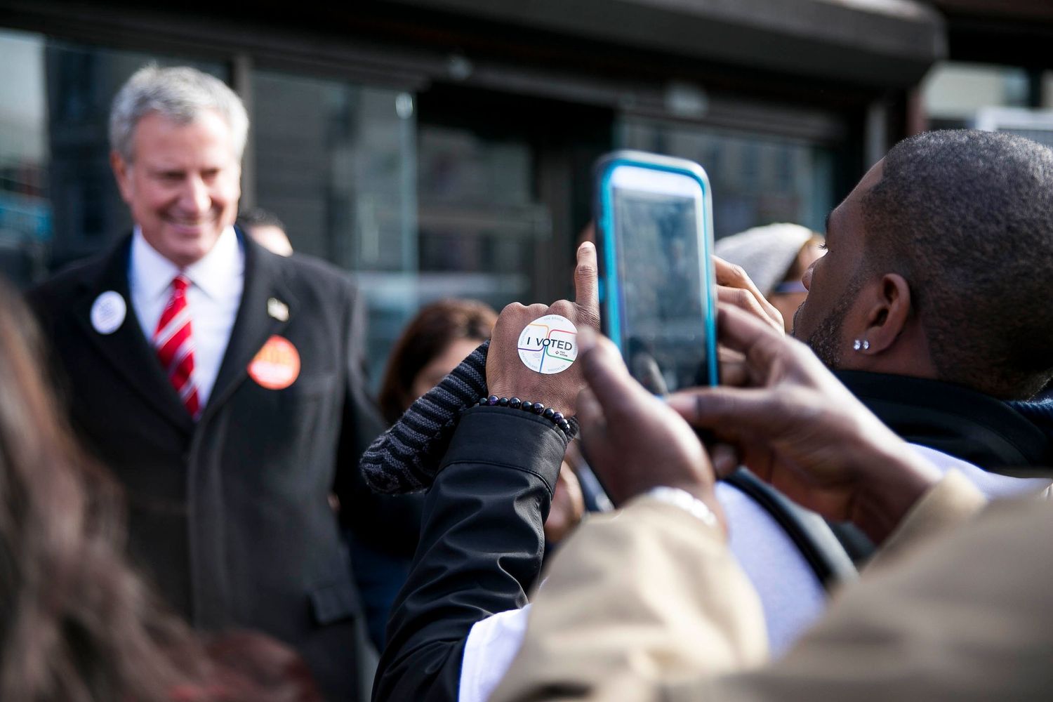 People gather in a crowd holding up phones and cameras to take pictures or recordings on their devices.