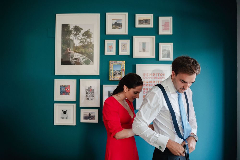 Two people getting dressed against a teal wall decorated with framed artwork.