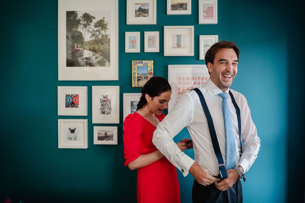 A couple wearing red and blue outfits shares a joyful moment against a turquoise wall with framed artwork.