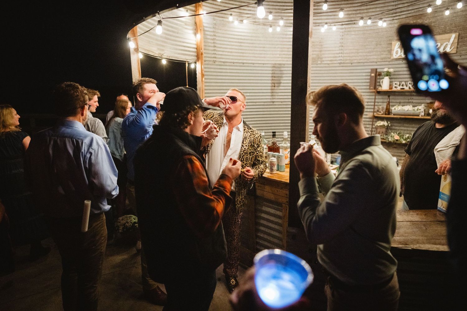 Large group of people socialize and mingle in a dimly lit indoor space decorated with string lights and panels.