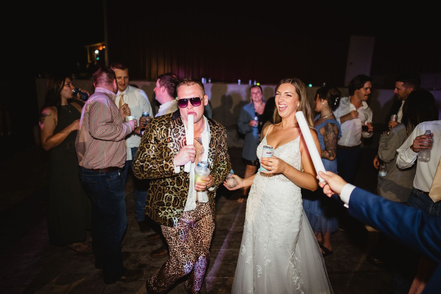 People dancing and celebrating on a dimly lit dance floor at a lively wedding reception.