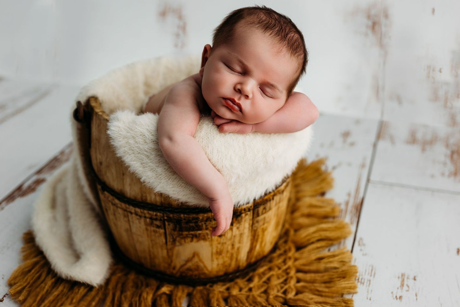 Sleeping newborn photographed lying on cozy textured brown blanket against light background.