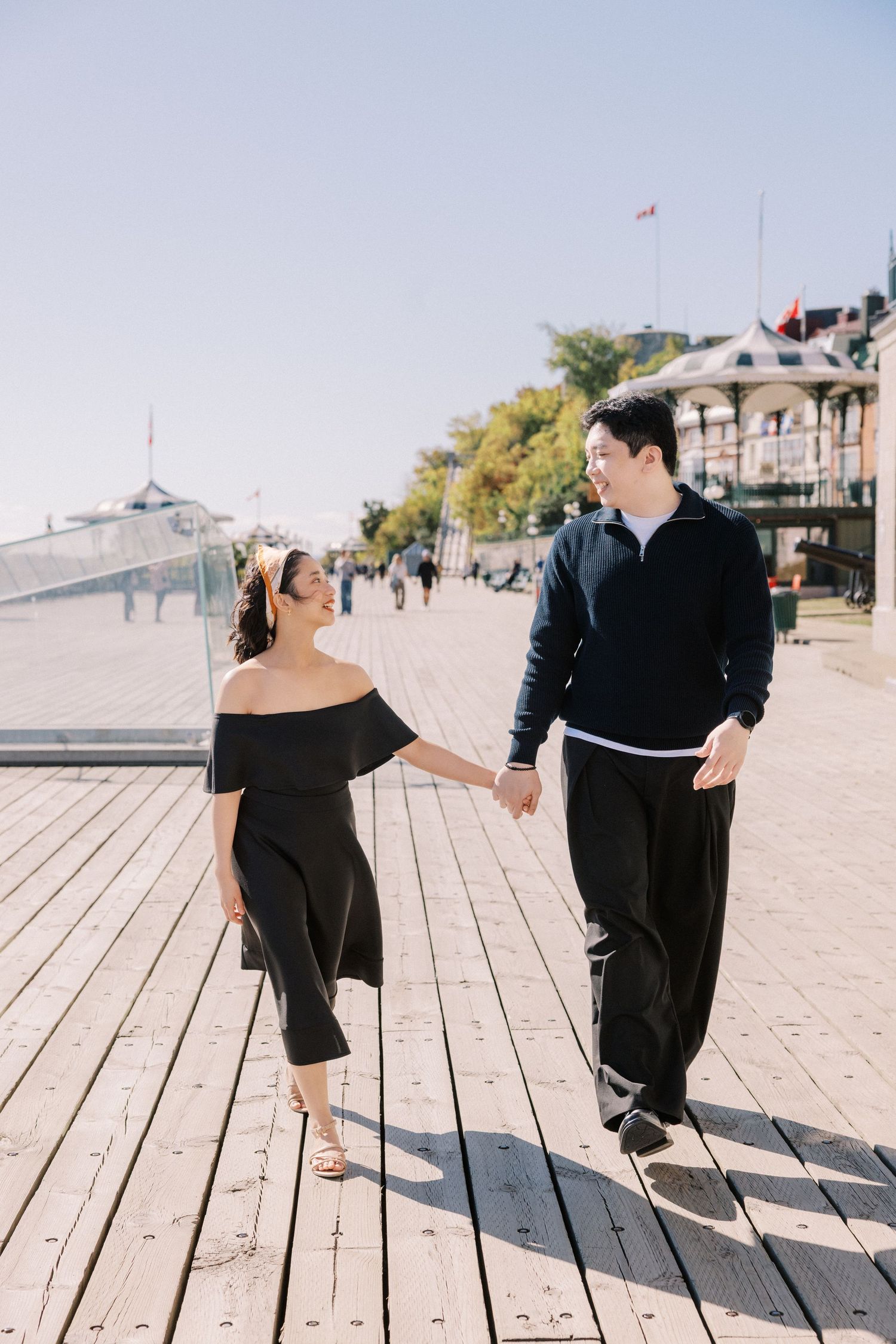 A couple in black outfits dance together on a wooden boardwalk on a sunny day, creating playful shadows.