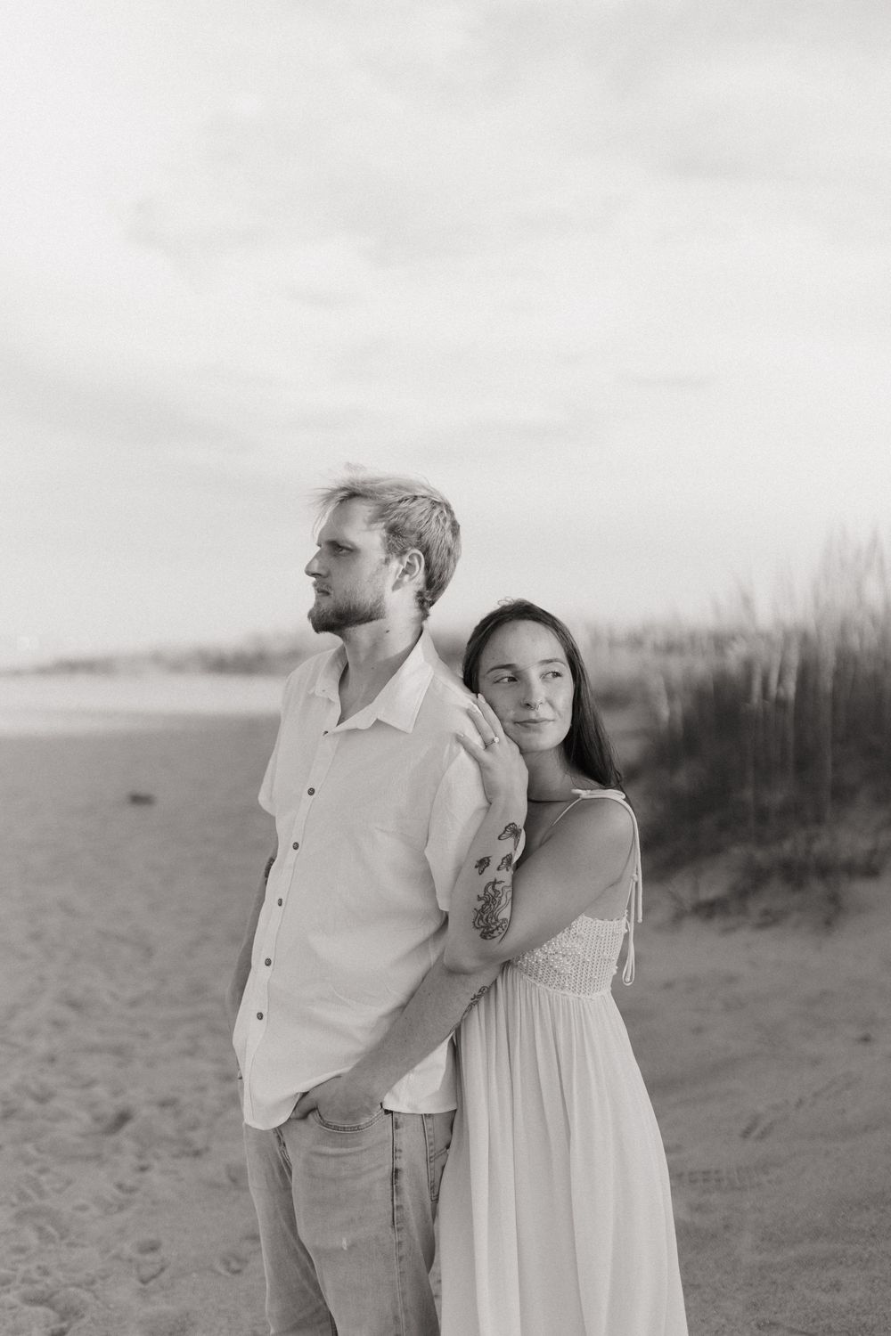 Black and white romantic beachside photo series showing tender moments between a couple on sandy dunes at sunset.
