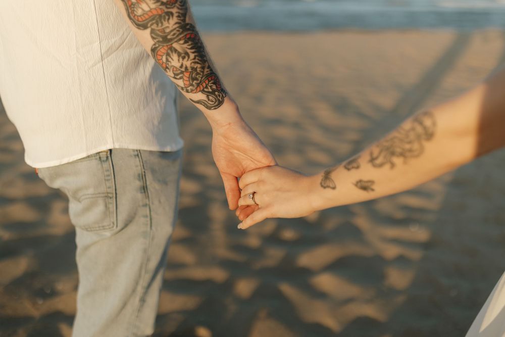 A group of people holding hands in a line walking together on a sandy beach at sunset.