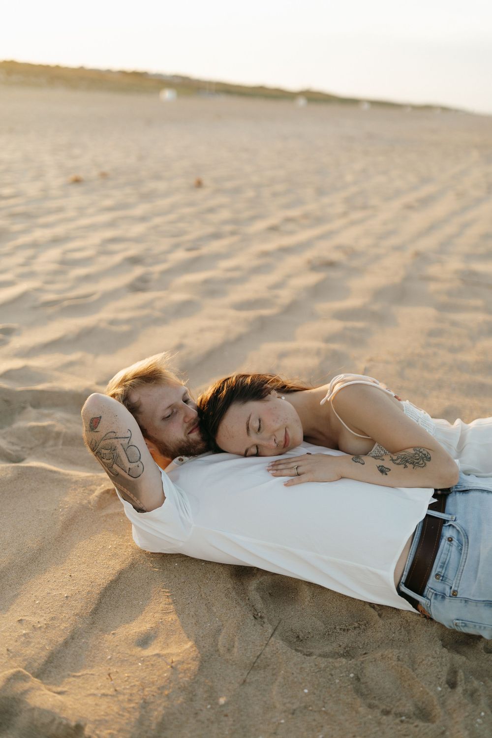 Person relaxing and lying down on a sandy beach at sunset with soft golden light casting warm shadows.