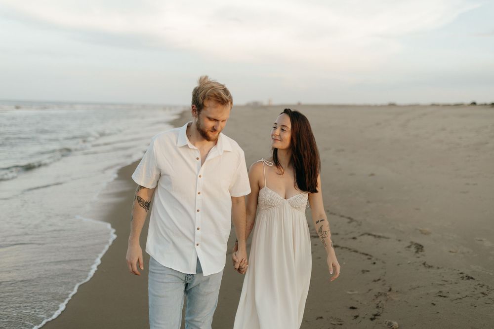 Couple walking together on a sandy beach at sunset while holding hands.