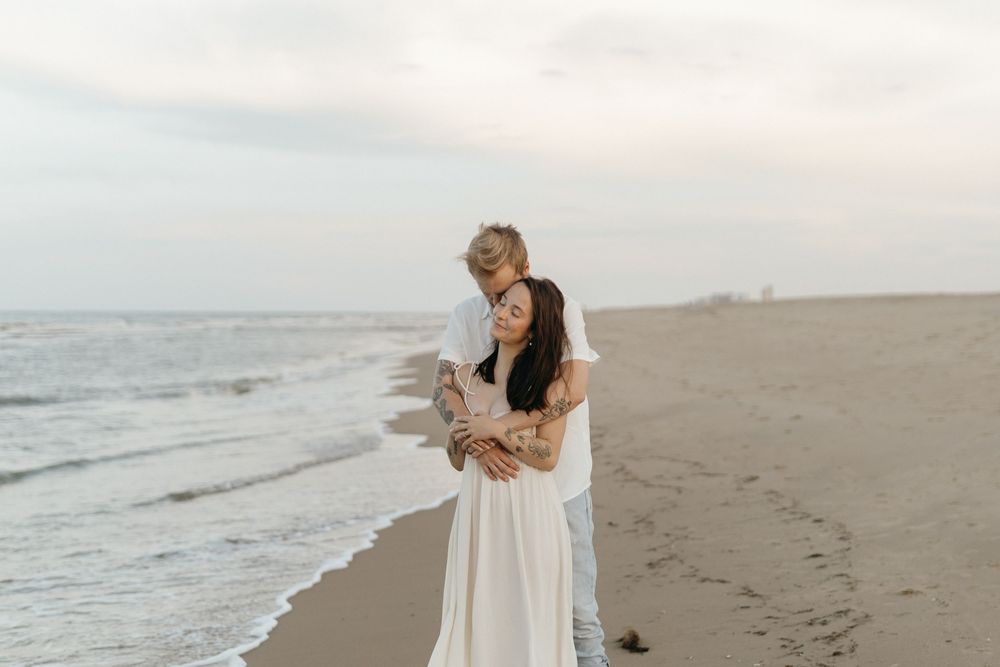 Two people embrace on a misty beach at sunset while waves roll onto the shore in the background.