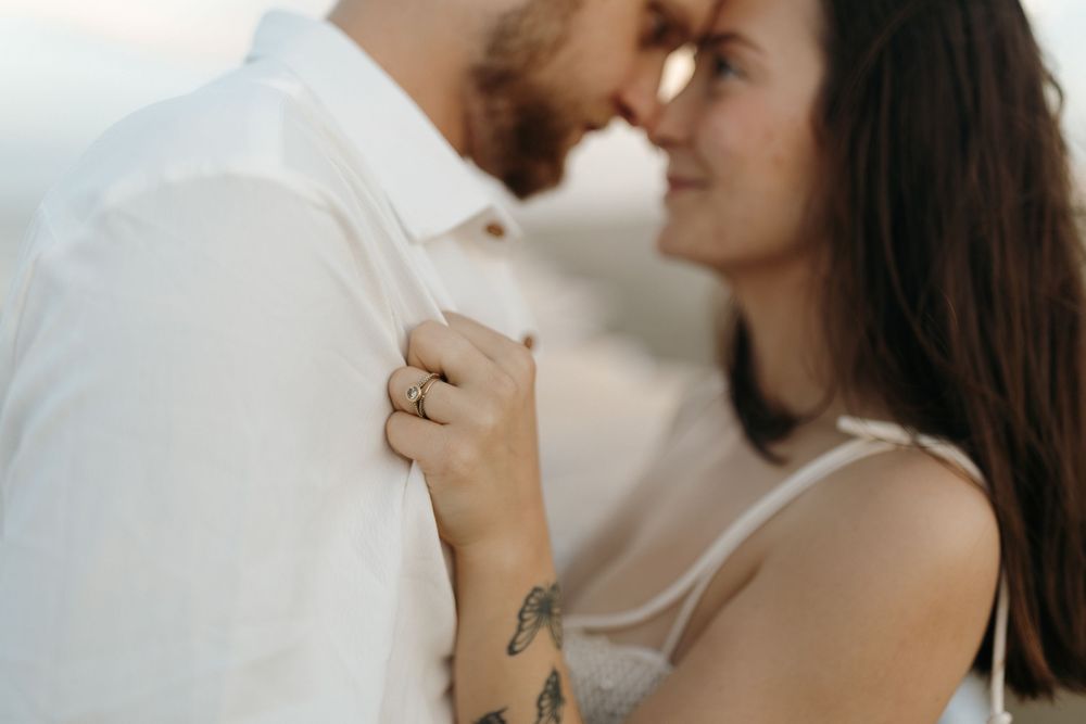 A stylish couple embraces lovingly while holding coffee mugs in a romantic indoor setting.