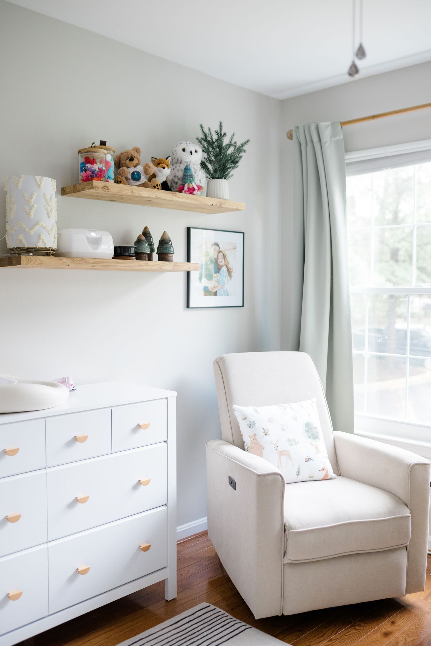 Modern nursery featuring white furniture, wooden shelves, and soft mint green curtains.
