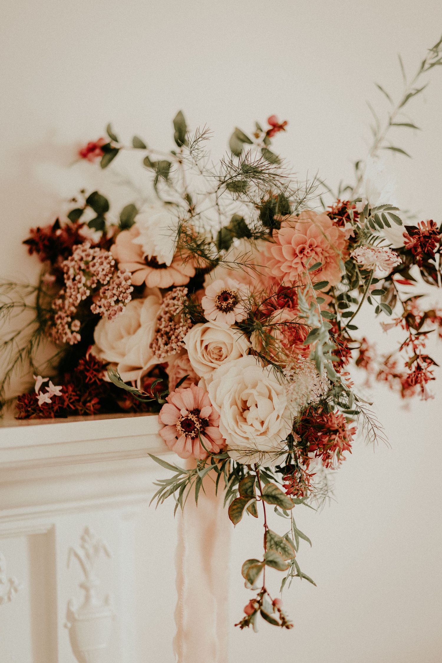Wedding reception decor featuring romantic floral arrangements of pink and peach roses adorning a white mantlepiece.