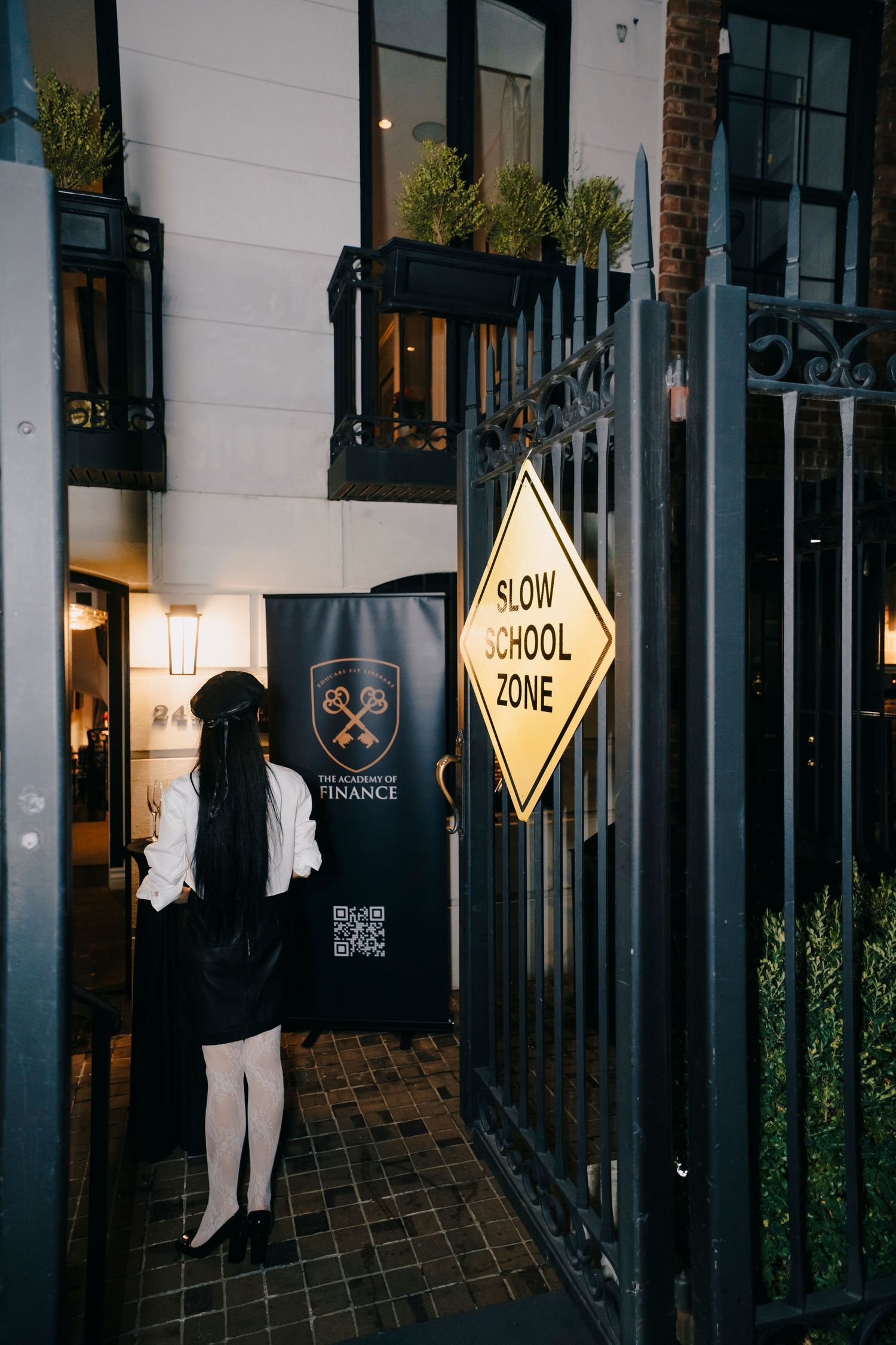 People walking past illuminated storefronts with slow zone warning signs on a dark evening street.