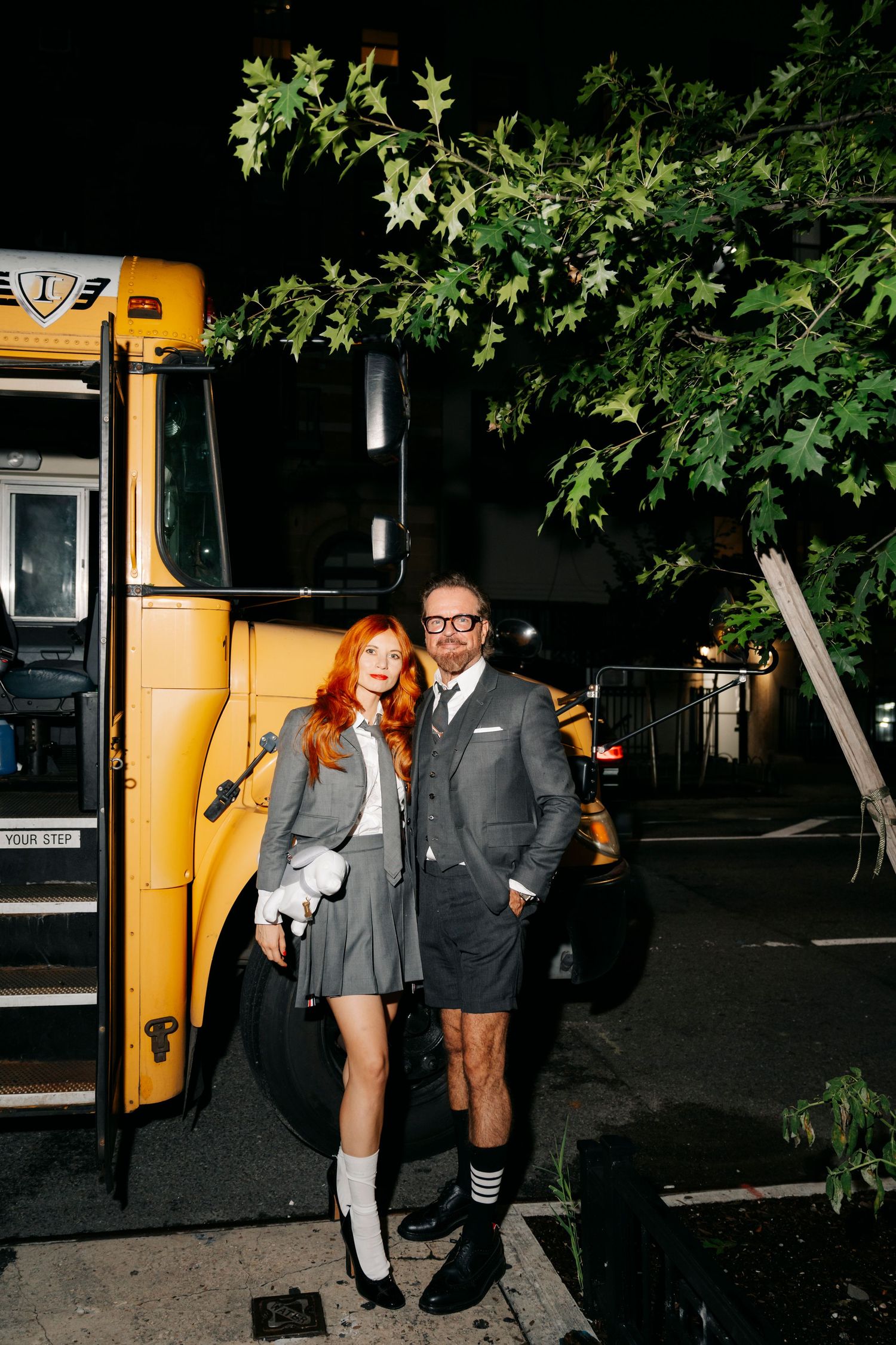 Couple poses in front of yellow school bus at night, creating a stylish retro-inspired photoshoot scene.