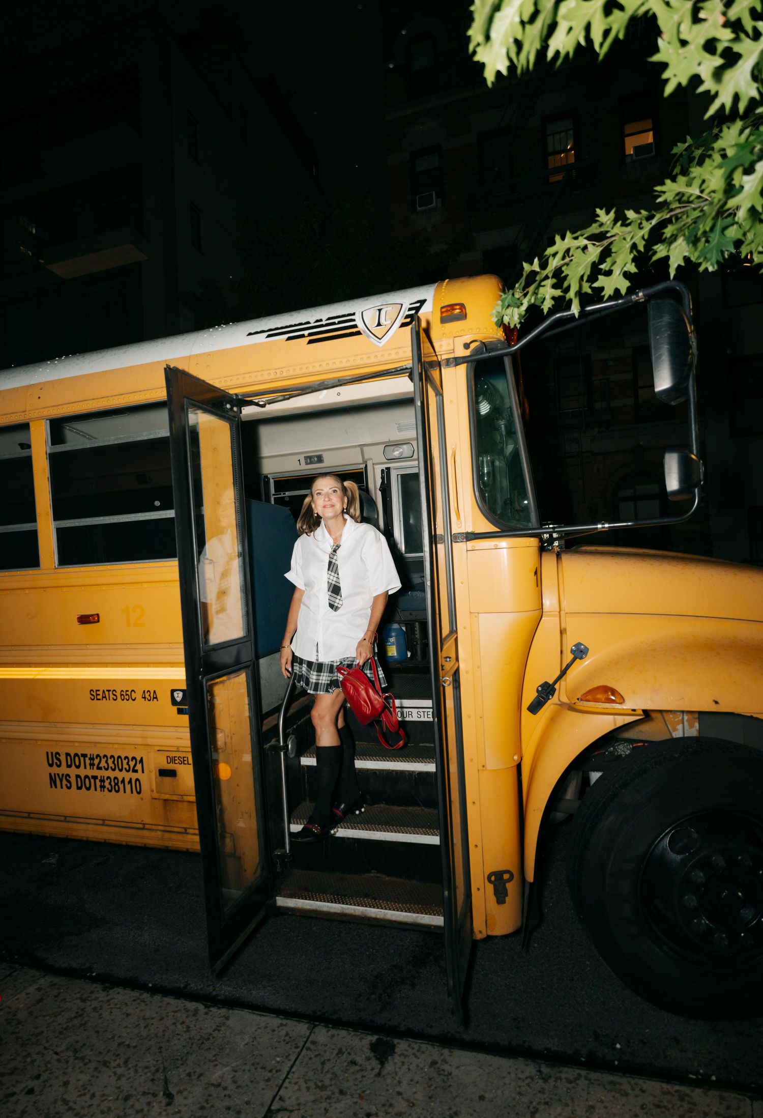 Person in casual attire stands in the doorway of a yellow school bus during an evening photoshoot.