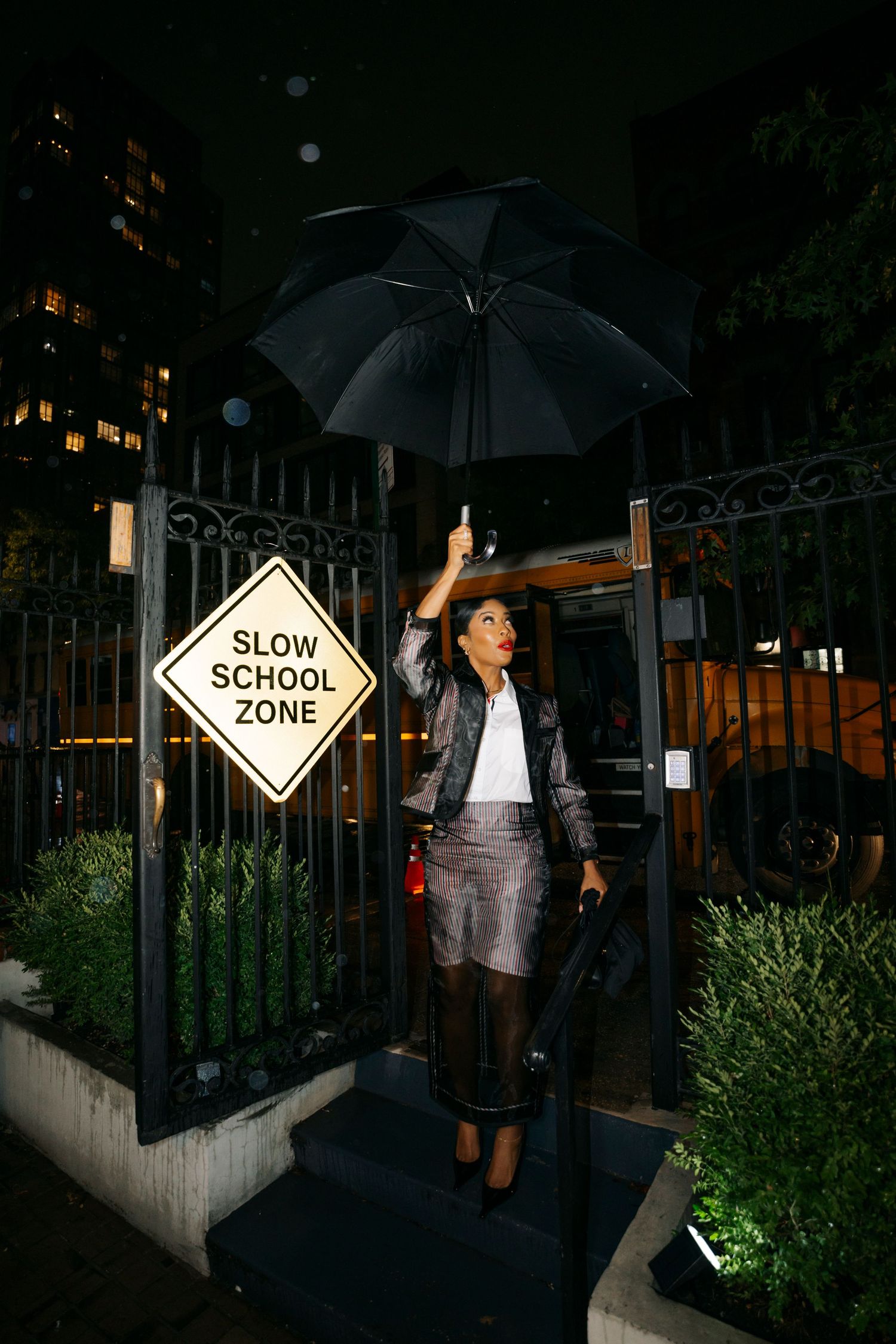 A person with an umbrella stands beside a slow school zone sign at night.
