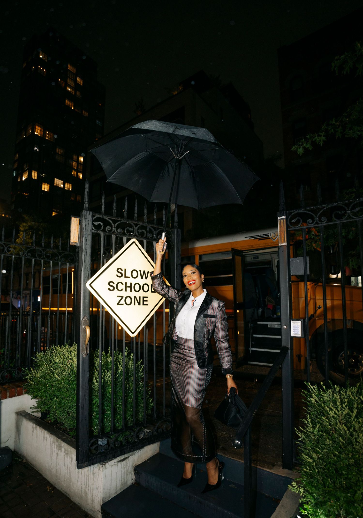 People walking at night near a school zone sign holding umbrellas.
