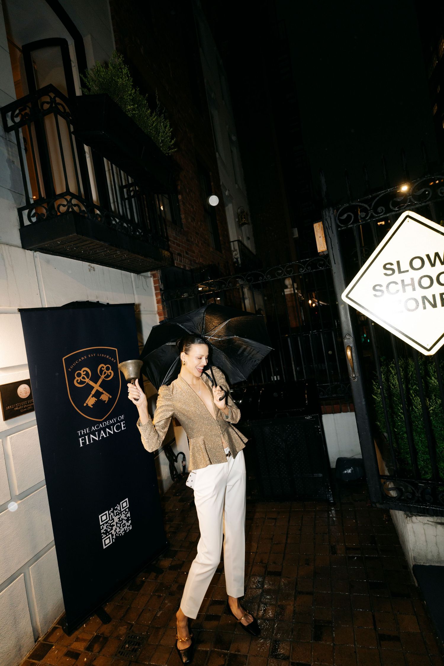 Person poses with an umbrella at night next to a slow sign and branded wall banner.