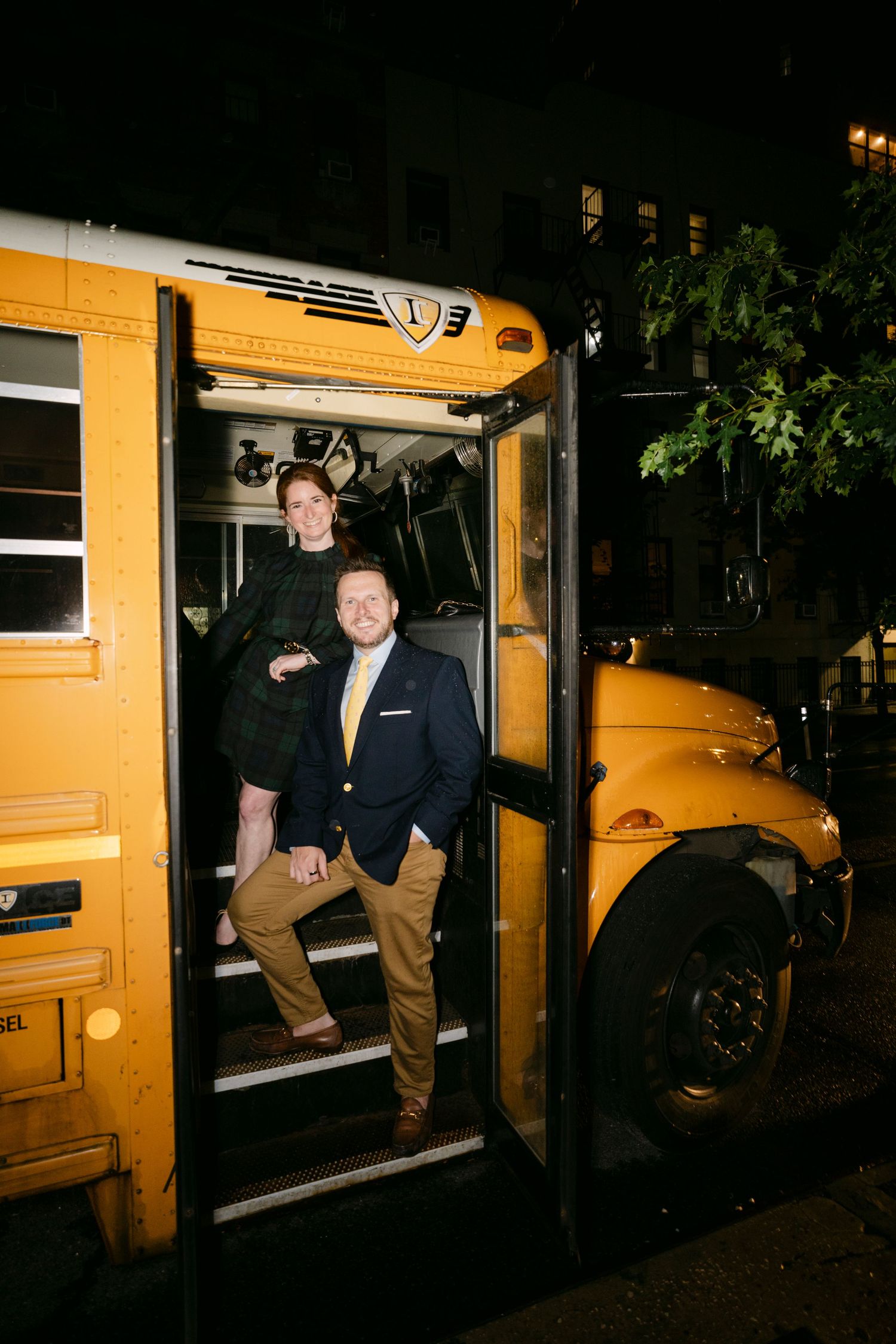 People posing and climbing around a yellow school bus at night.