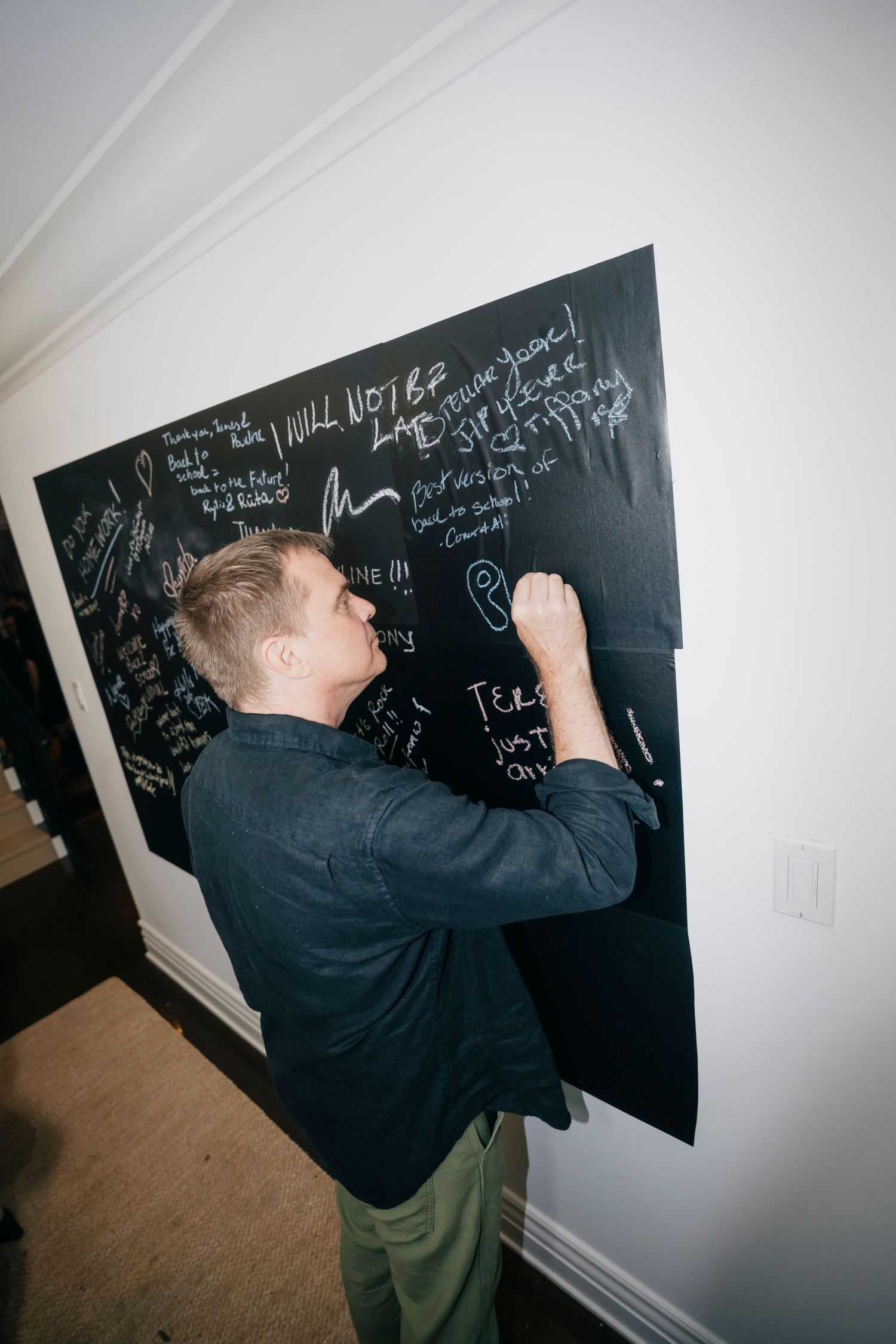 Person writing mathematical equations on a black chalkboard wall.