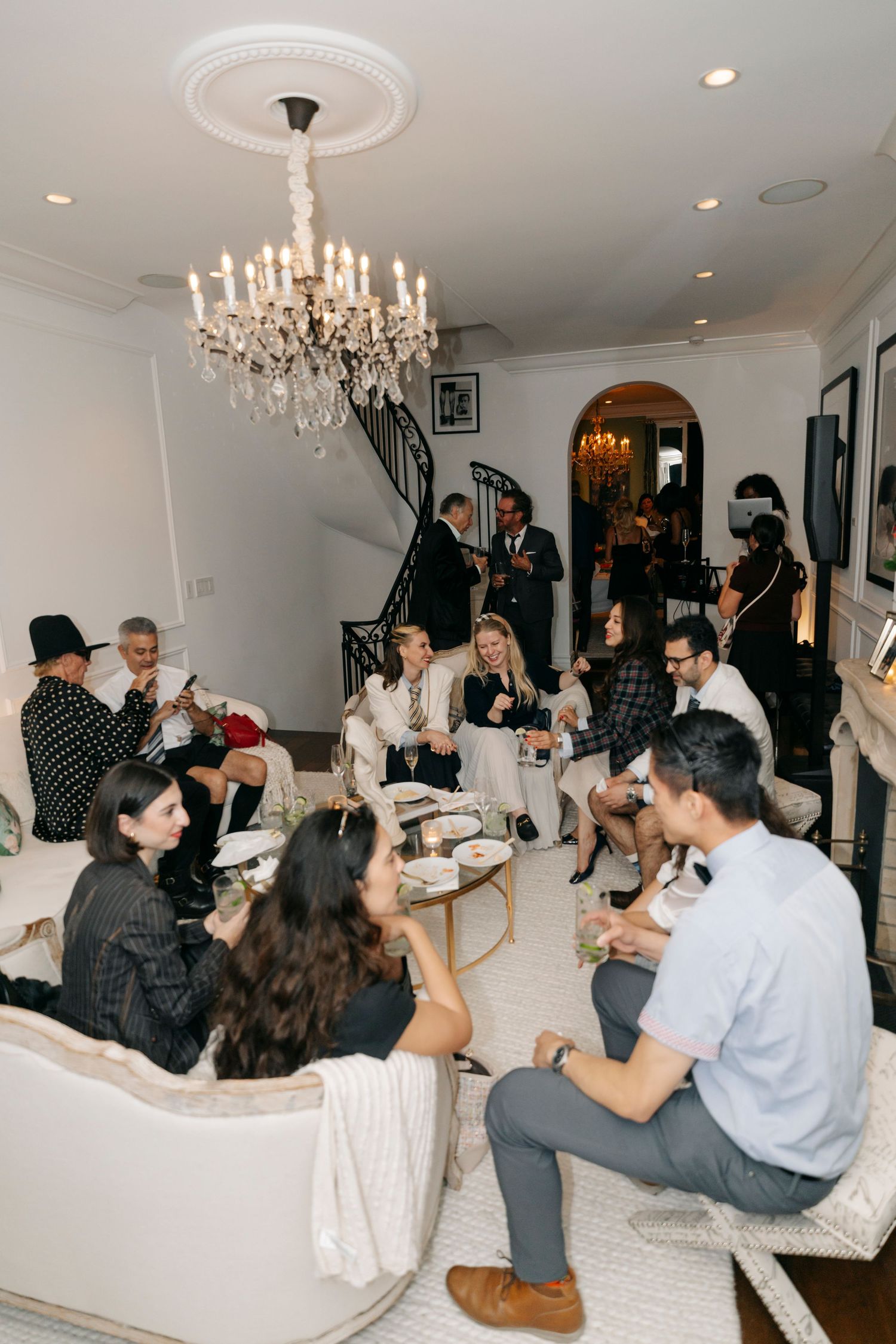 Group gathering in an elegant white room with chandeliers during a party.