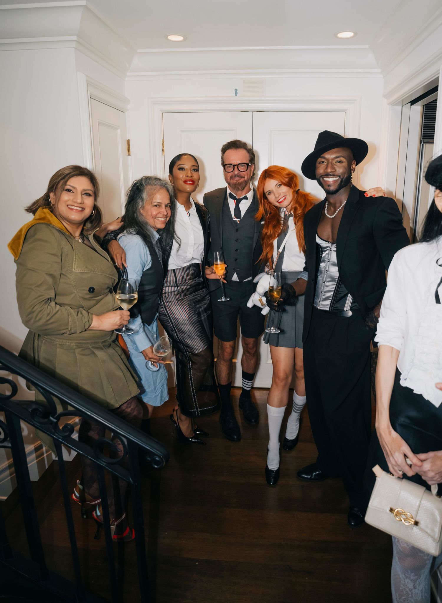 Group gathered indoors wearing mix of formal and casual attire on dark hardwood floors.