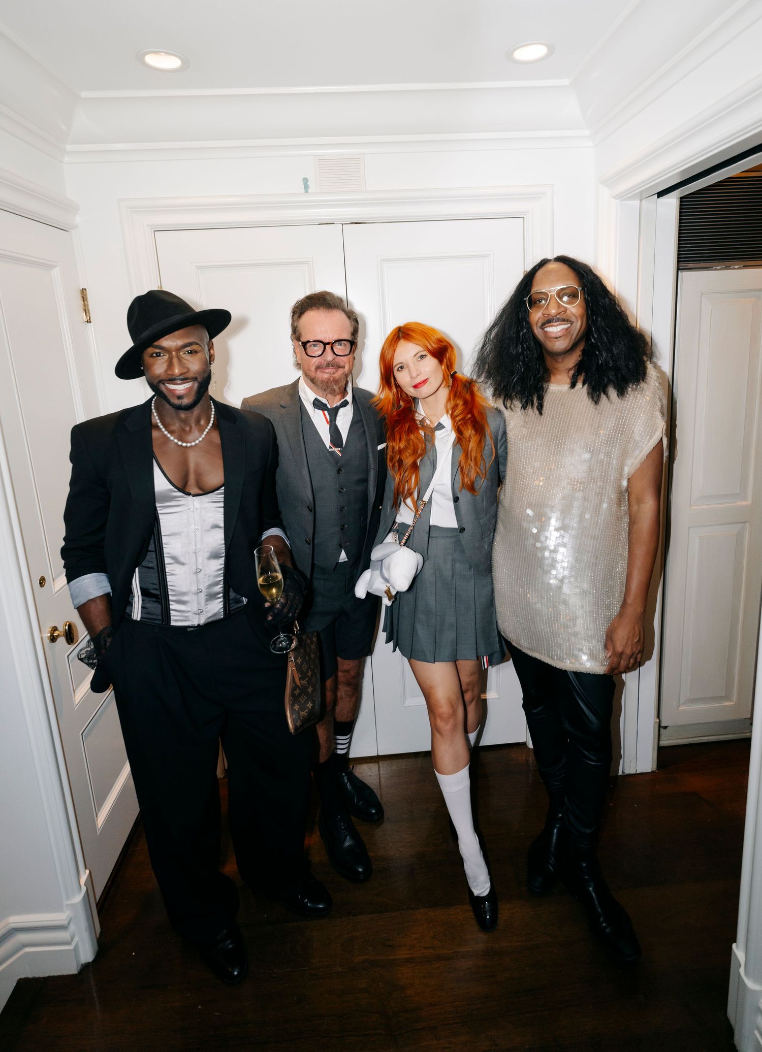 Group of people in formal attire and costumes posing together in a white hallway.
