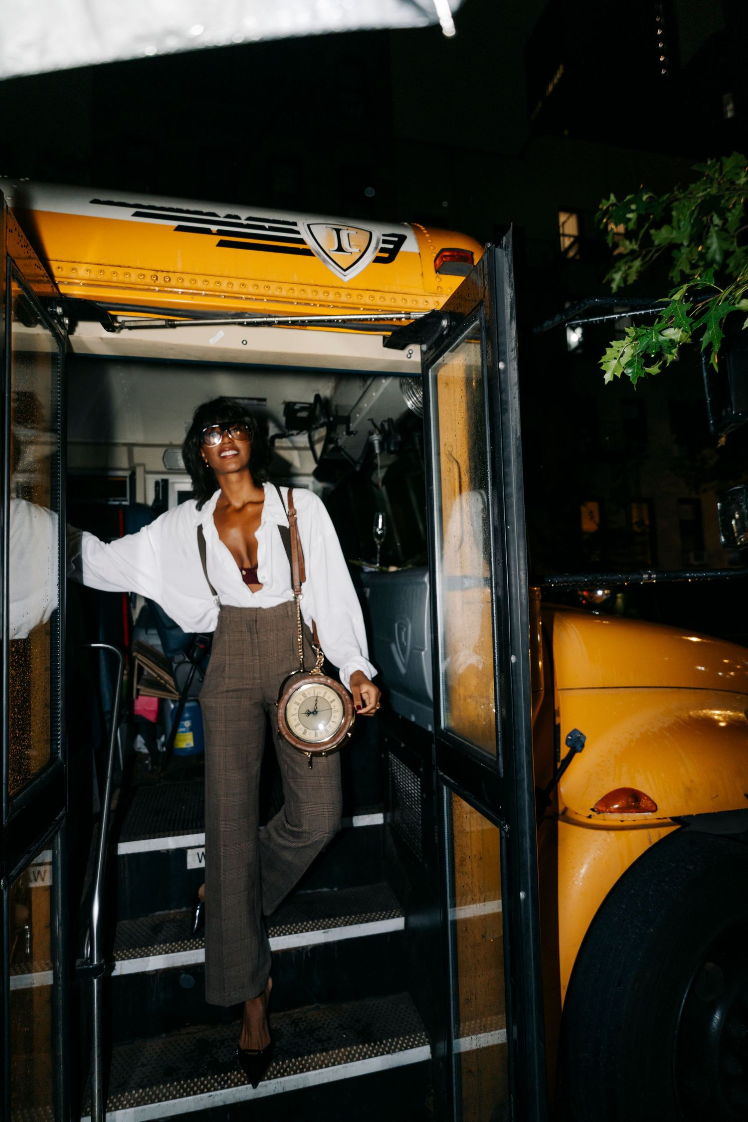 People in vintage-style outfits enter and exit a bright yellow school bus at night.