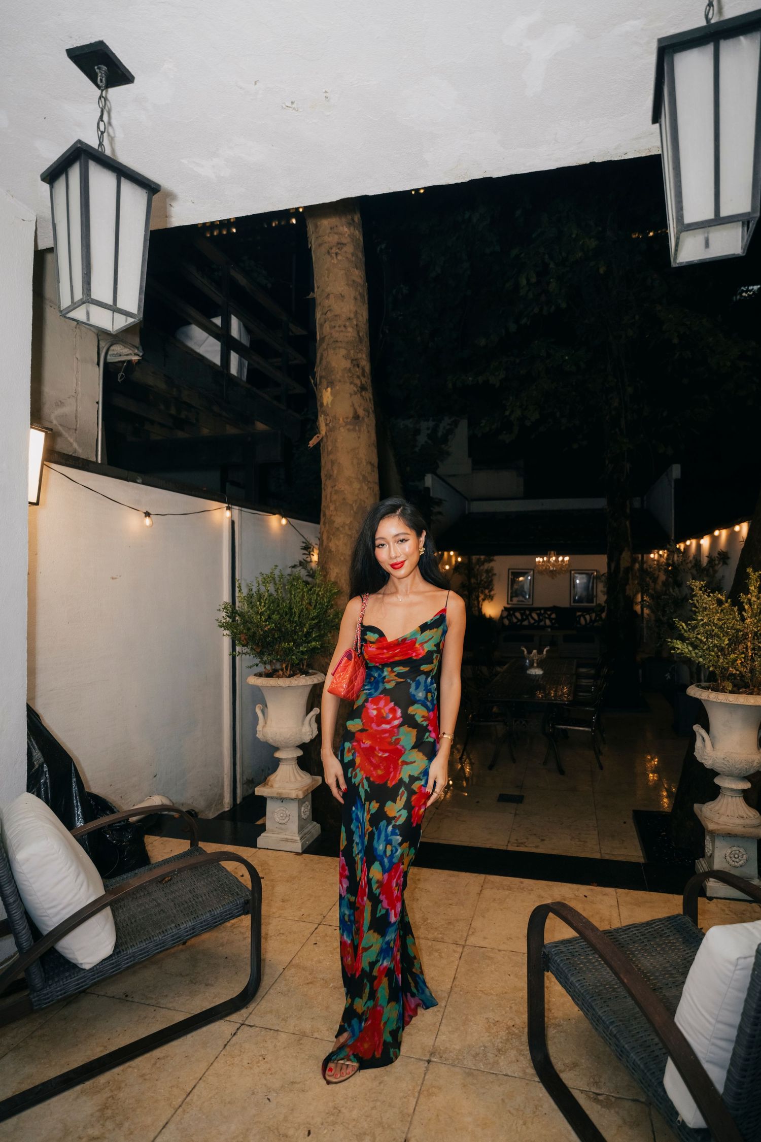 Person in floral dress poses against outdoor patio setting with lanterns at night.
