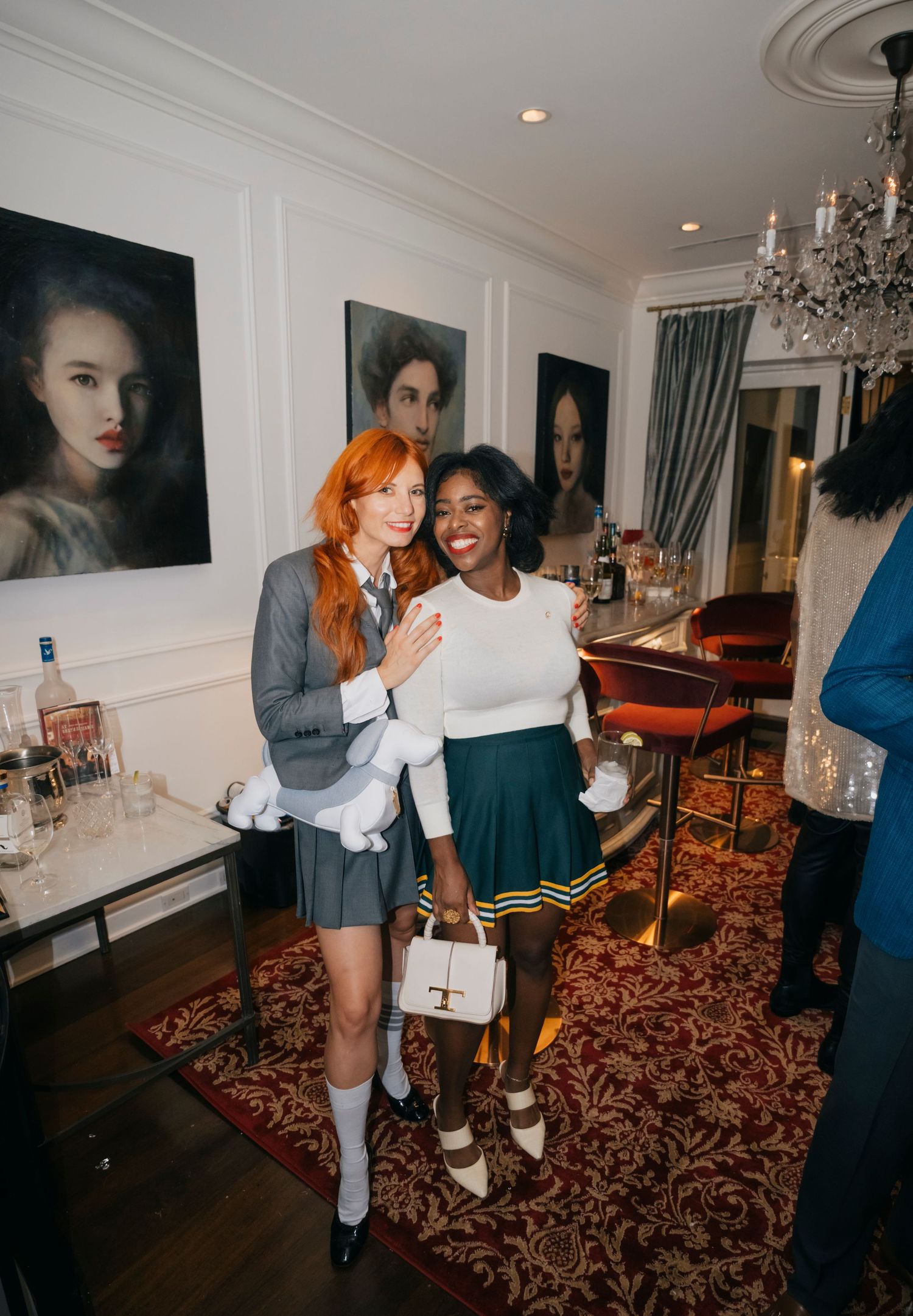 Two friends share a joyful moment together in an elegant room decorated with vintage portraits and a crystal chandelier.