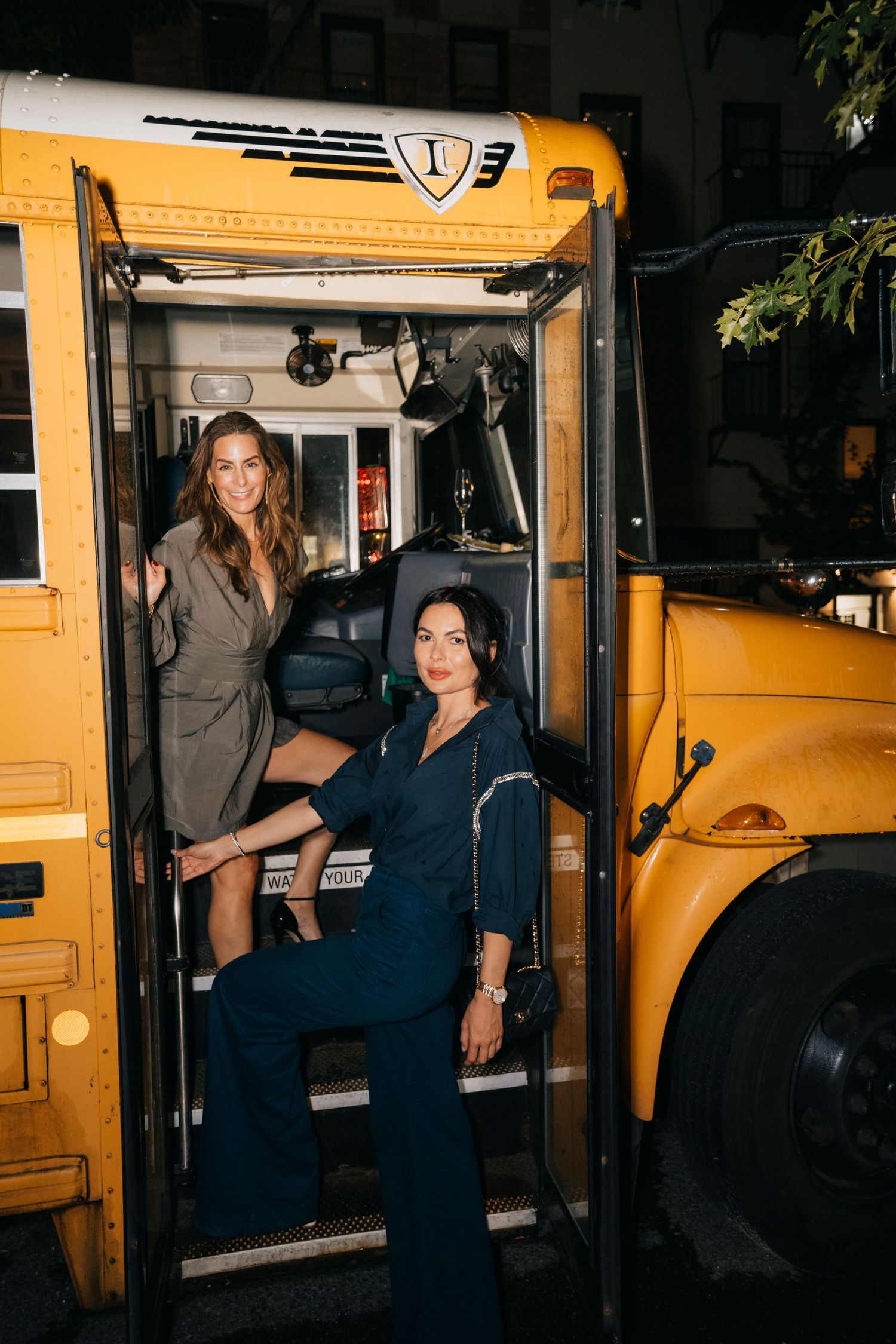 Several people stand near open door of yellow school bus in dark setting.