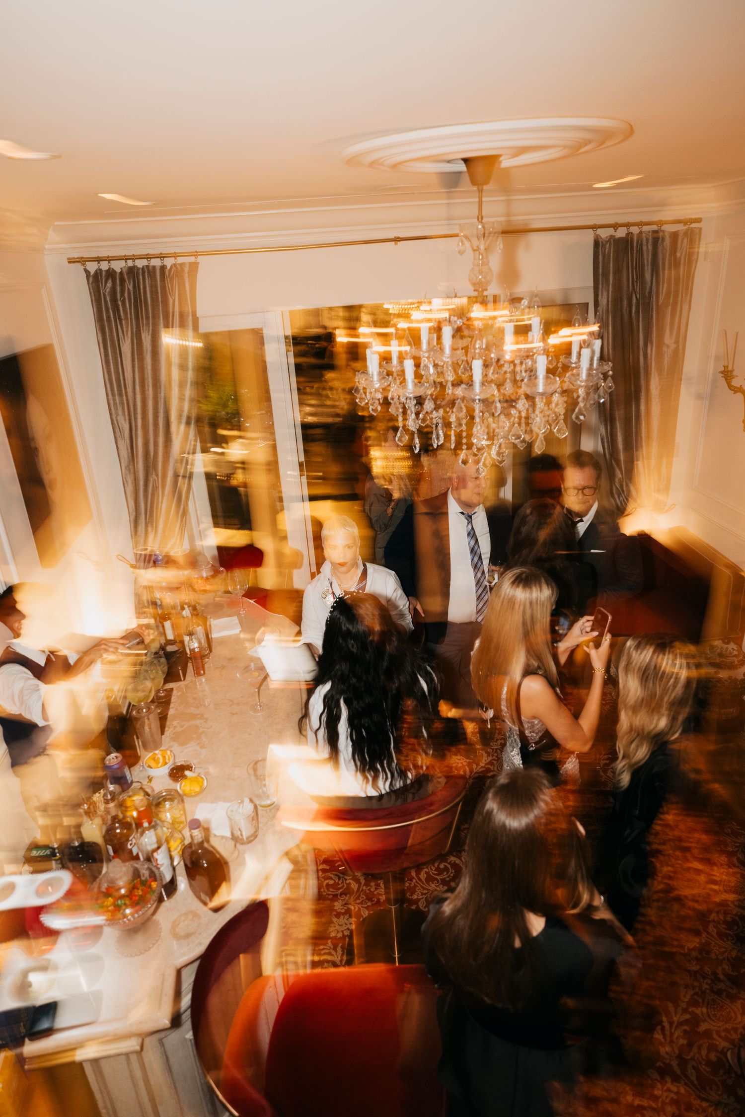 Blurred motion shots of people dancing at an elegant indoor party with chandeliers.