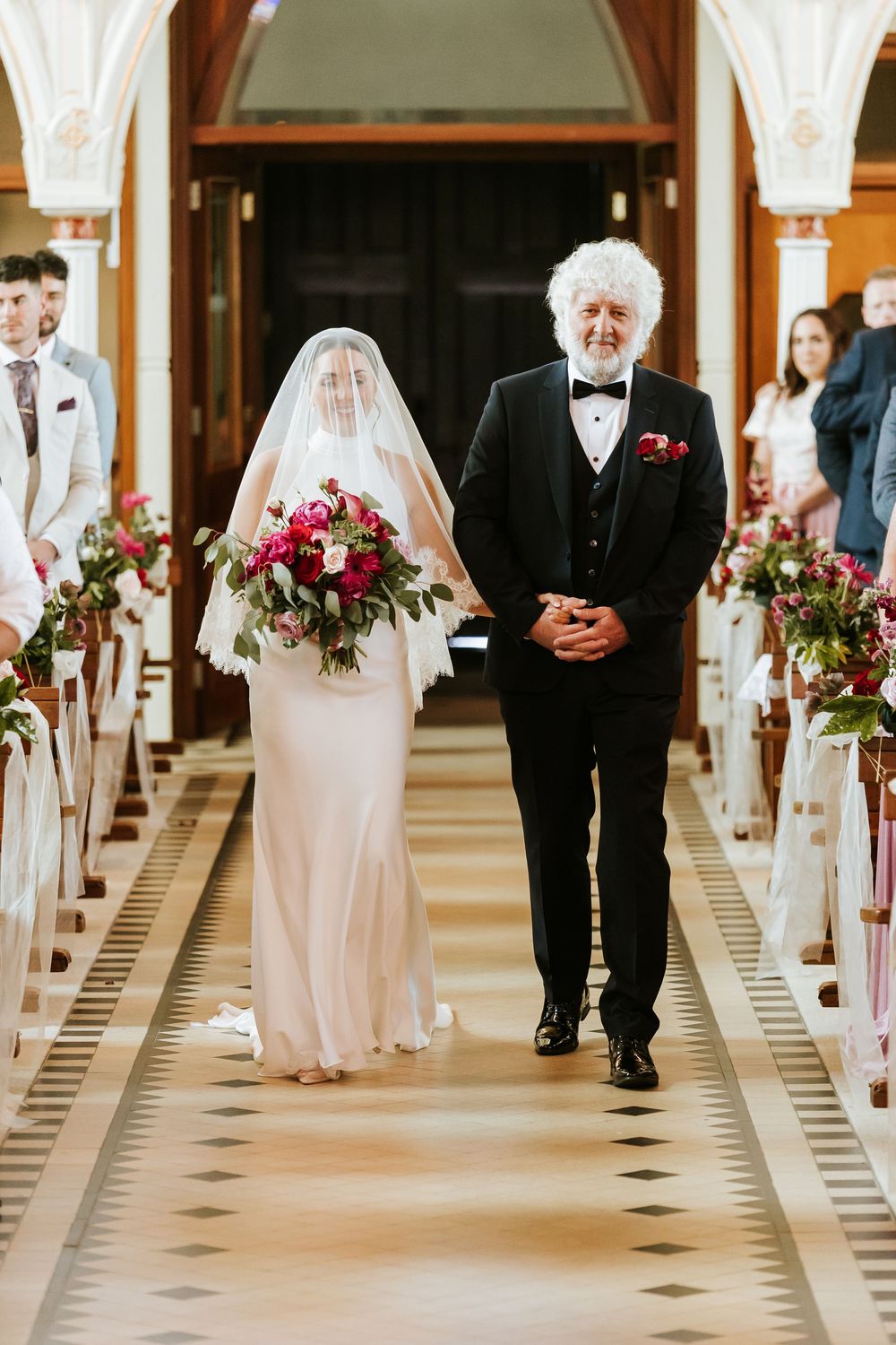 People in wigs and white outfits walk down an ornate hallway at an elegant dinner venue.