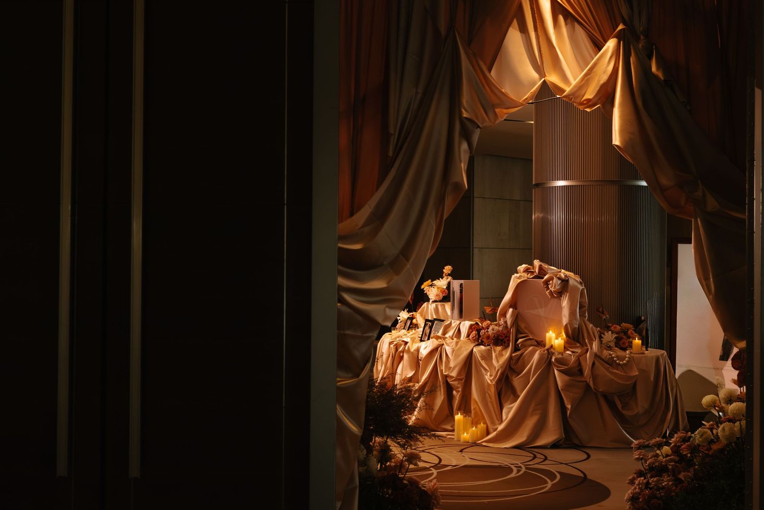 Opulent golden draped curtain wedding reception setup with candlelit table and floral decorations.