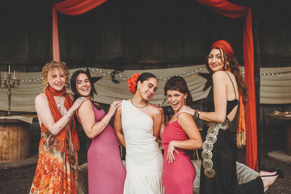 Wedding party dances and celebrates under red fabric draping at a reception venue during festivities.