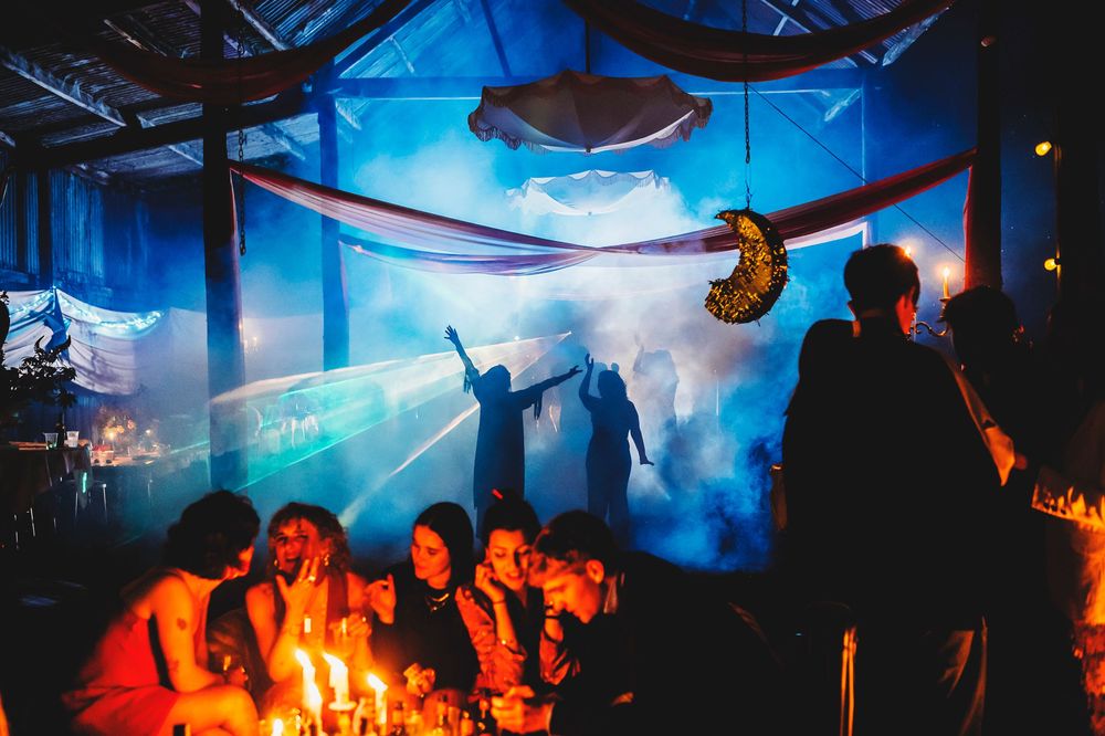 Silhouettes of concert crowd dancing under blue stage lighting and glowing effects at a nightclub event.