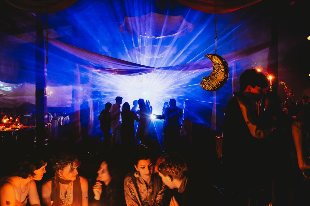 Blue and orange lights illuminate a dark nightclub dance floor with silhouettes of people dancing in a festive atmosphere.