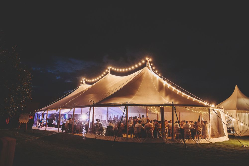 Large white outdoor event tent illuminated with warm string lights creating a magical evening atmosphere at night.