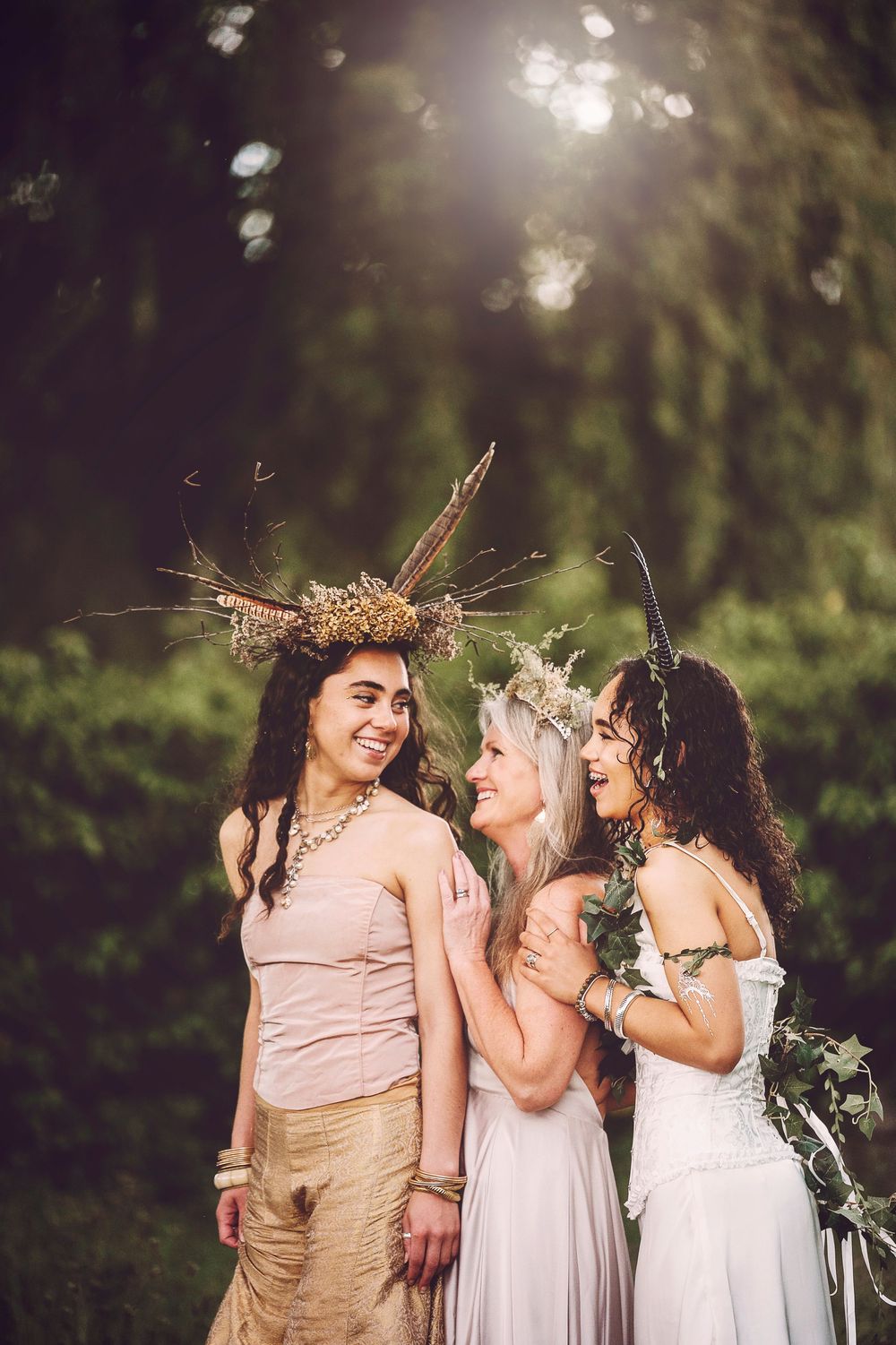 A group wearing floral crowns and flowy dresses laugh together in a dreamy outdoor garden setting.